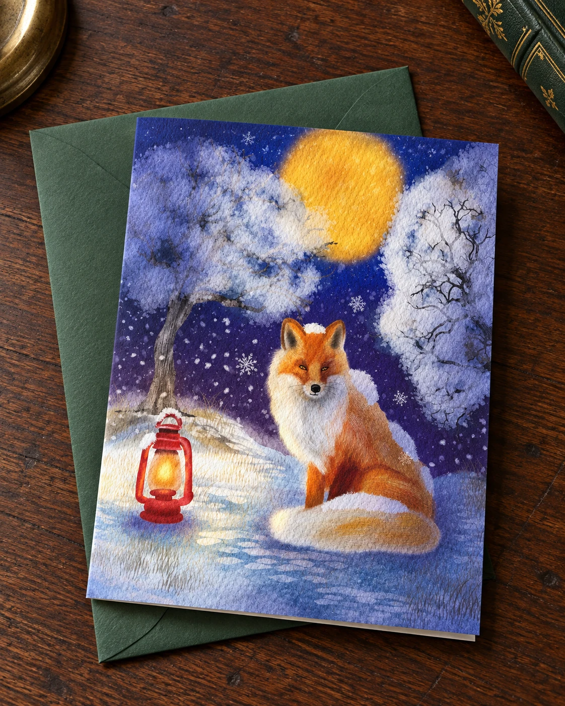 A Light in the Snow borderless 5 × 7 inch greeting card on a green envelope on an oak desk